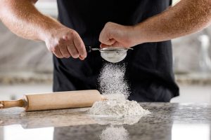 Select Chef  male chef sifting flour and a wooden rolling pin.